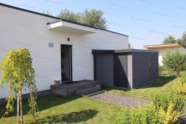 Montovaný záhradný domček v tmavosivej omietke pri bielom rodinnom dome