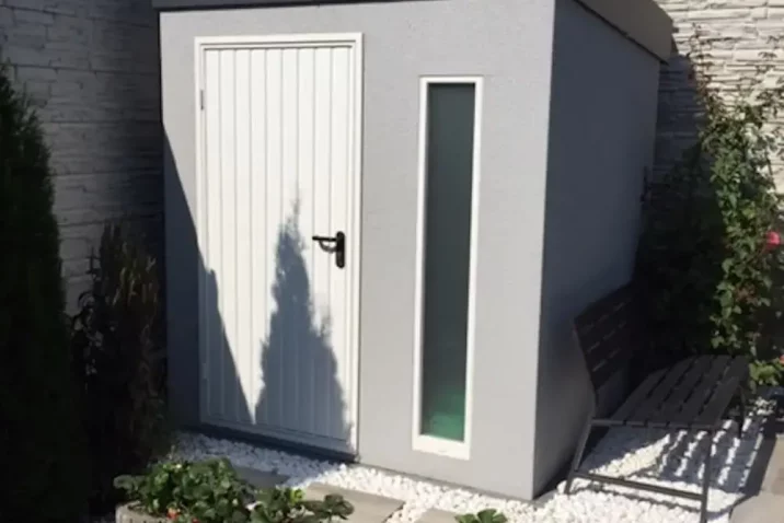 Záhradný domček v sivej omietke s bielymi dverami a bielym svetlíkom