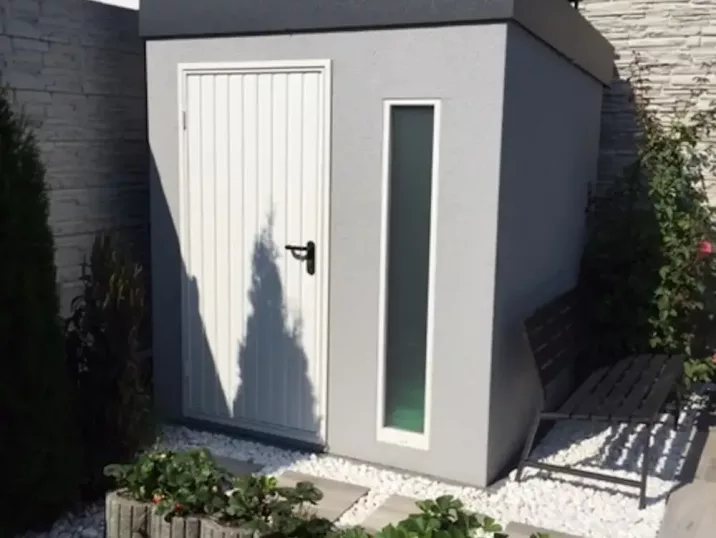 Záhradný domček v sivej omietke s bielymi dverami a bielym svetlíkom