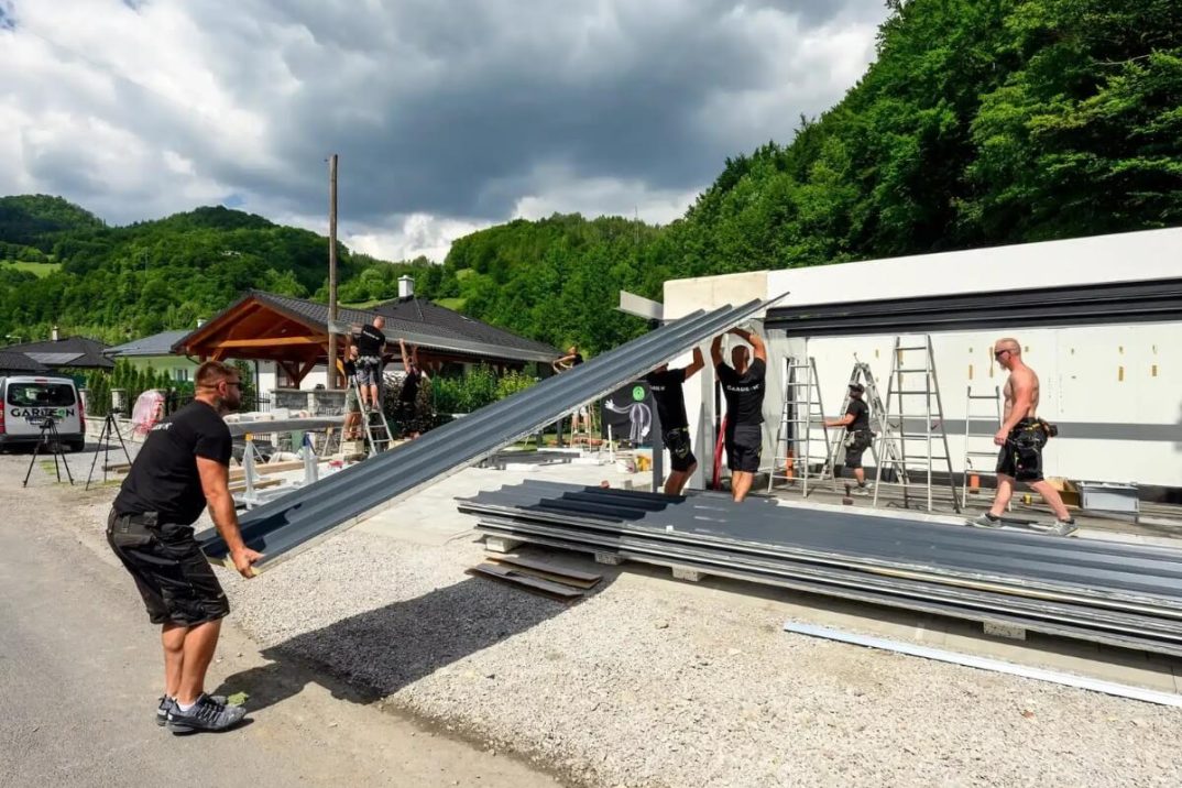 Montážnici vykladajú strešnú krytinu na strechu.