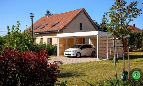 Prístrešok pre dve autá s bielou strechou medzi stromami v záhrade.