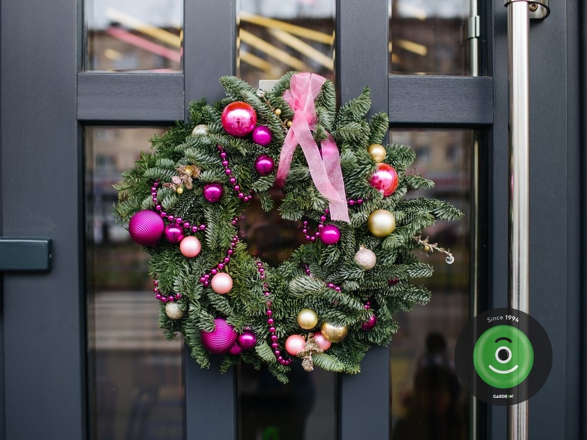 Vianočný veniec na dverách s ružovými dekoráciami.