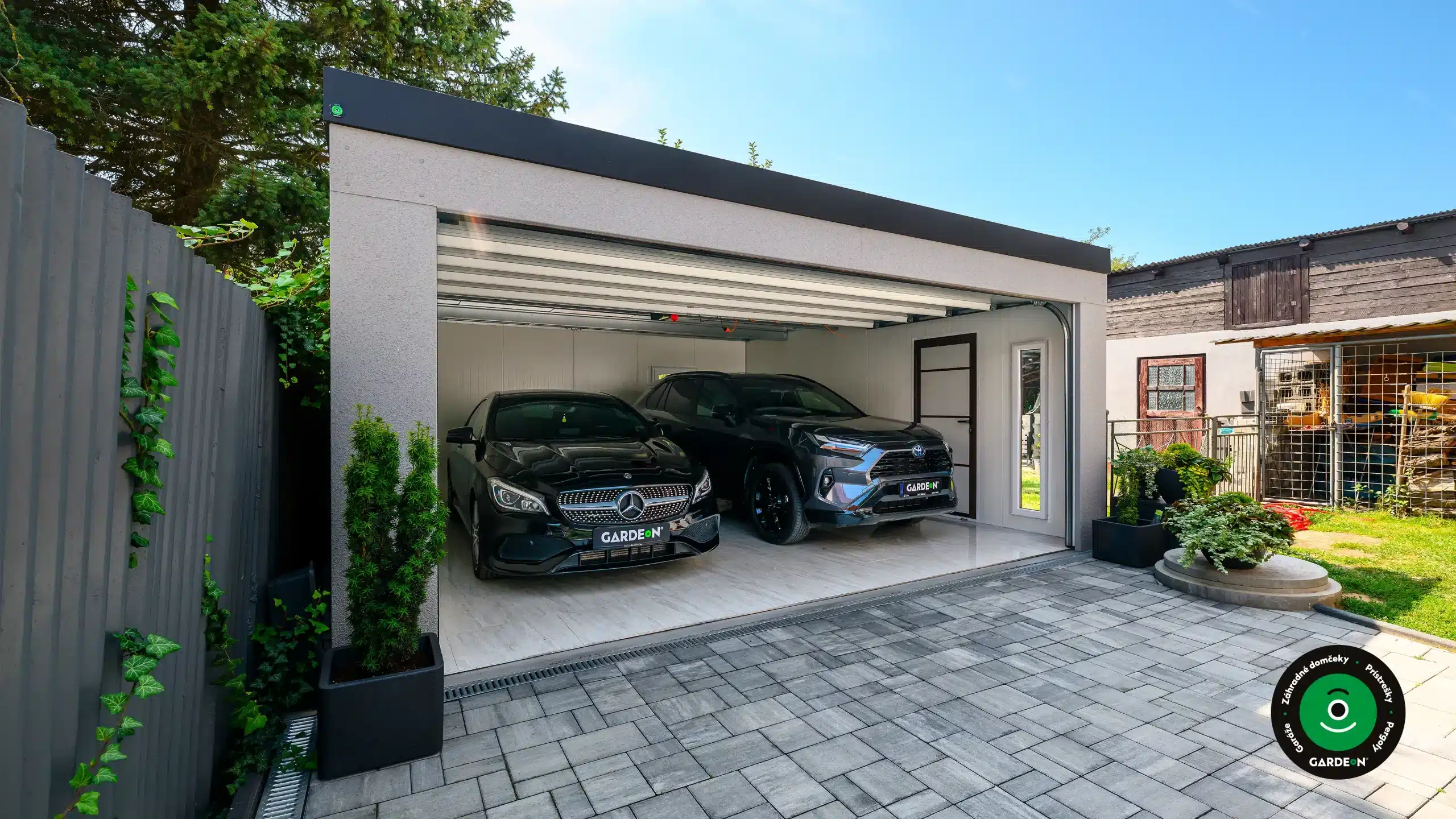 Dvojgaráž s otvorenou bránou a dvomi vozidlami.