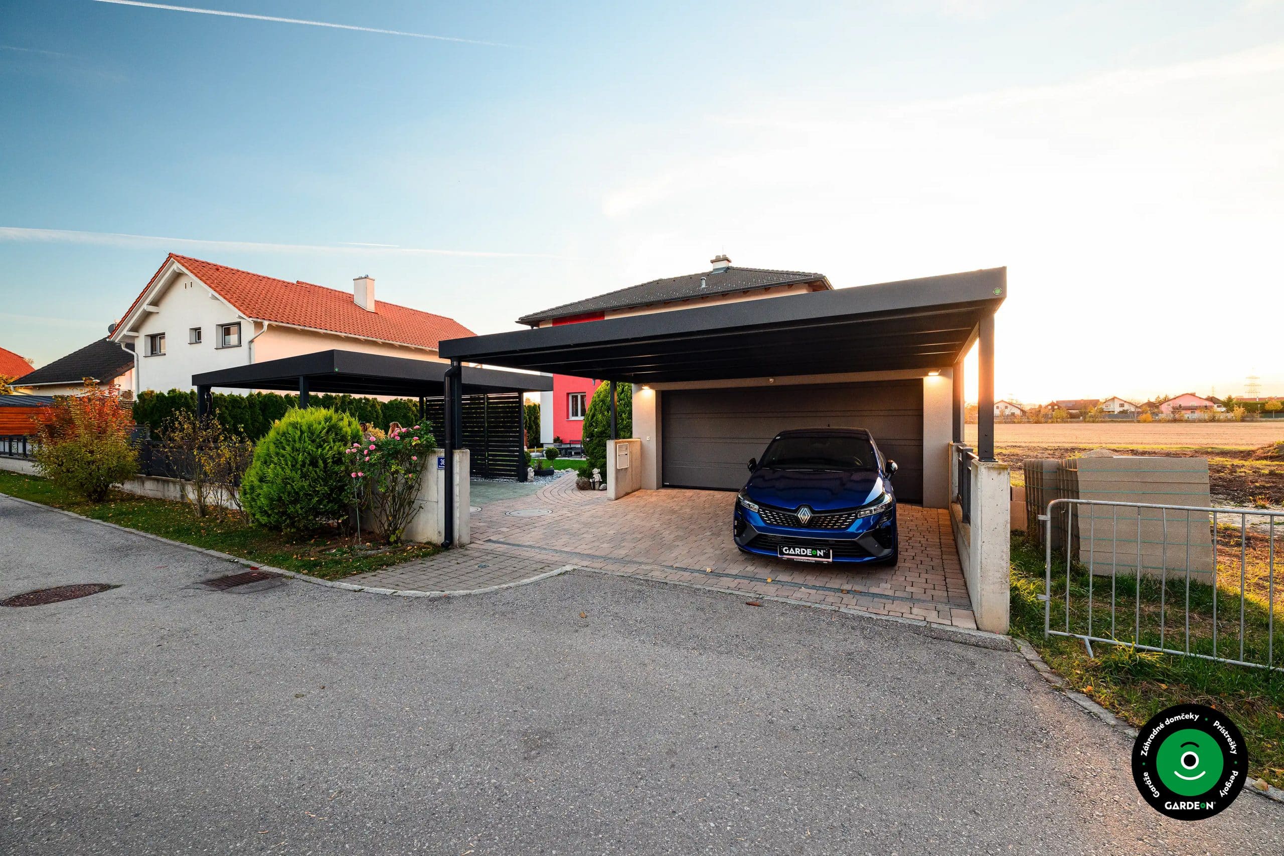 Moderná garáž s prístreškom pri dome s upravenou predzáhradkou a kríkmi
