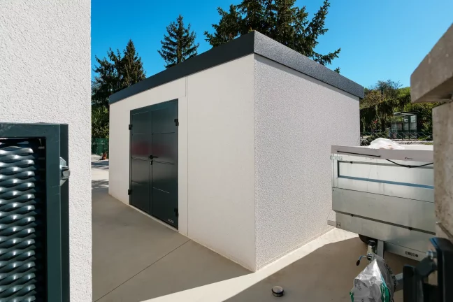 Minimalistický záhradný domček s prestrešeným priestorom vedľa rodinného domu