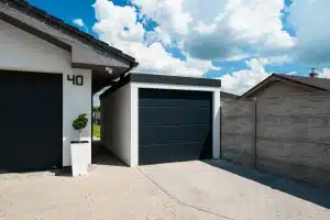 Detail bielej garáže s antracitovou pultovou strechou, tmavá sekčná brána