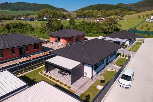 Letecký pohľad na pergolu s plochou strechou pri bielom rodinnom dome, zelené okolie s horami