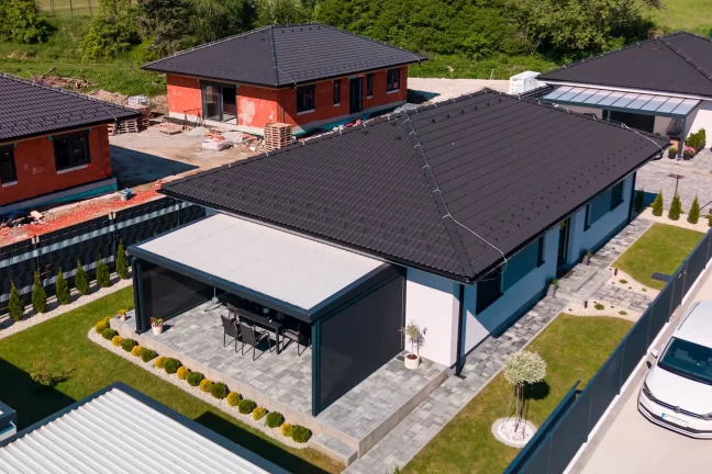 Letecký pohľad na pergolu s plochou strechou pri bielom dome, upravená záhrada s tujami