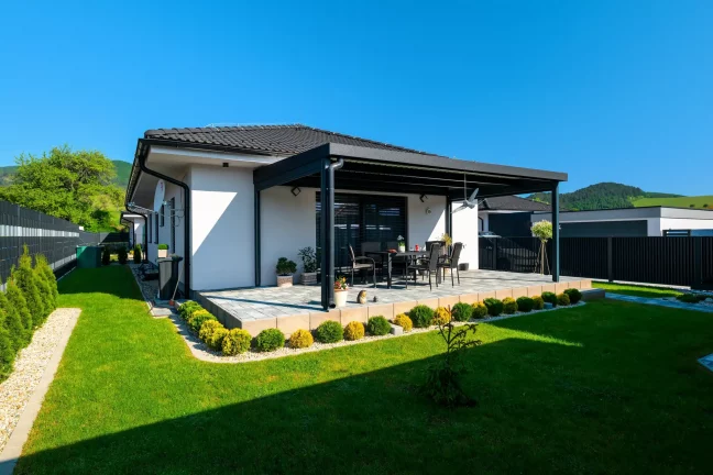 Pergola s antracitovou konštrukciou pri bielom dome, zelený trávnik