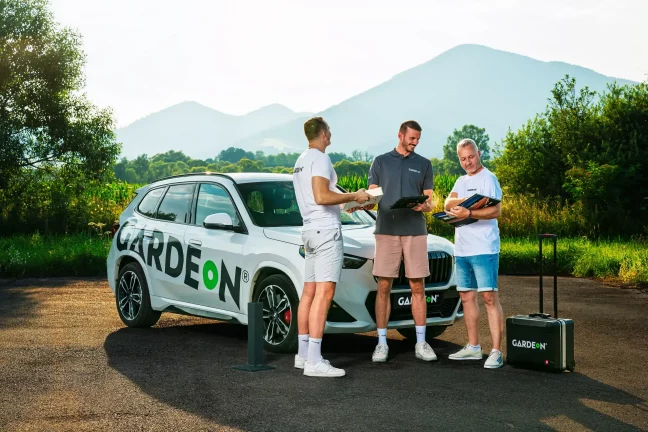 Konzultácia troch agentov GARDEON s podkladmi pri firemnom BMW v prírode.
