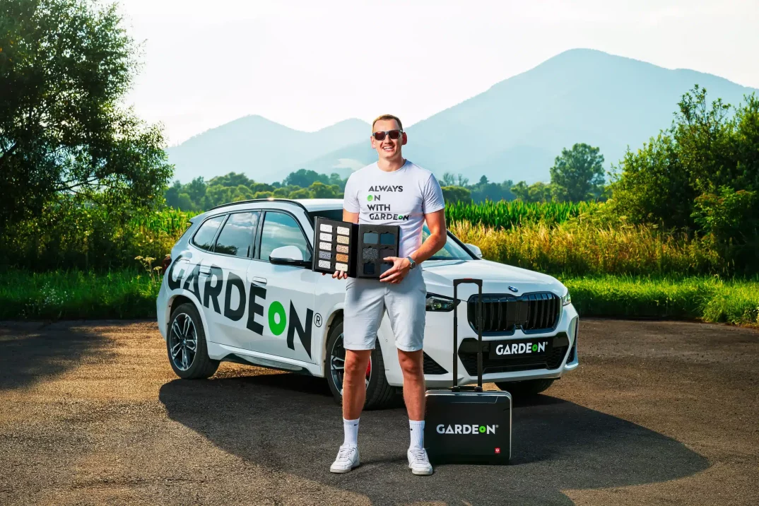 Obchodný agent, ktorý drží vzorkovník omietok pred firemným BMW v prírode.