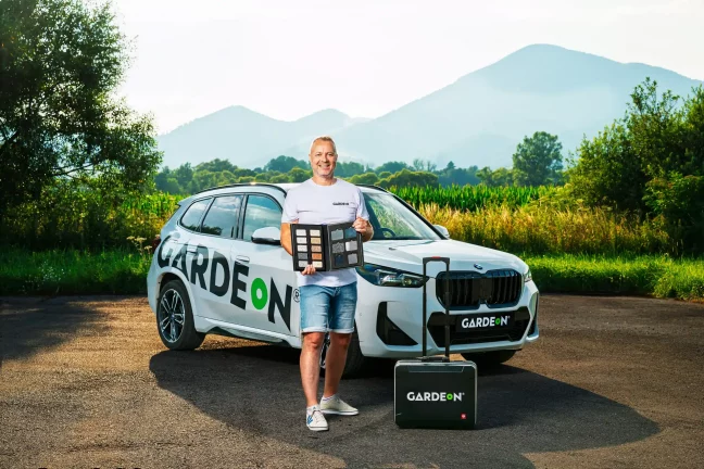 Úsmevný agent GARDEON so vzorkovníkom povrchov stojí pri firemnom BMW.
