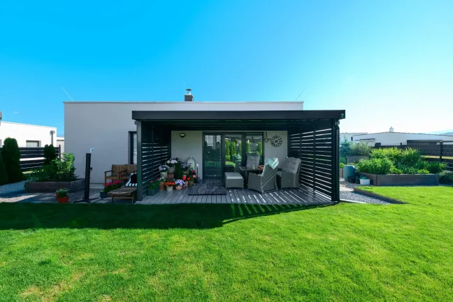 Antracitová pergola s kovovou výplňou pri rodinnom dome s trávnatou záhradou.