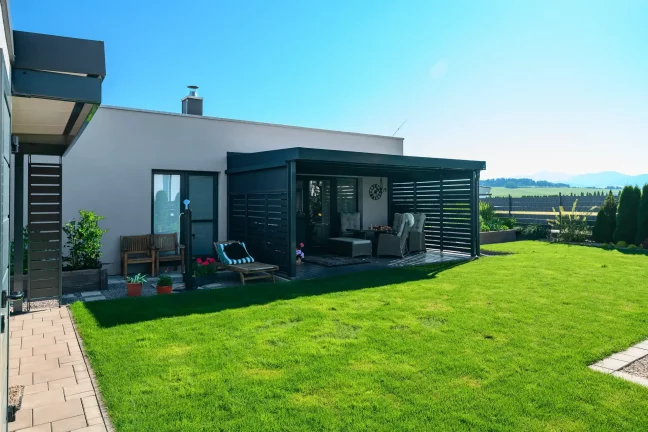 Antracitová pergola s kovovou výplňou pri rodinnom dome so záhradou.
