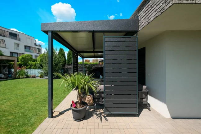 Antracitová pergola s bočným obkladom pri tehlovom dome, dekoratívne rastliny na terase