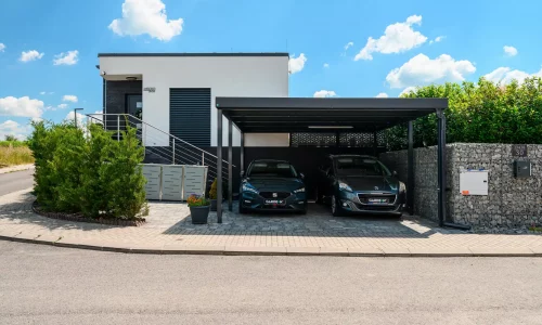 Prístrešok s antracitovou plochou strechou a s bočnou výplňou pri modernom dome.