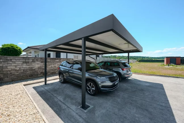Plochá antracitová strecha prístrešku chráni dve SUV pri rodinnom dome.