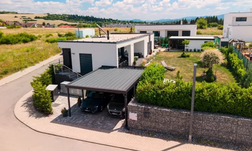 Vzdušný pohľad na dvojmiestny prístrešok s antracitovou plochou strechou pri modernom bungalove.