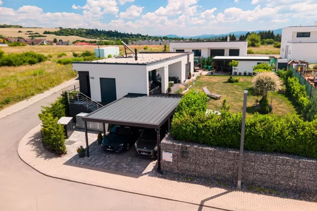 Vzdušný pohľad na dvojmiestny prístrešok s antracitovou plochou strechou pri modernom bungalove.