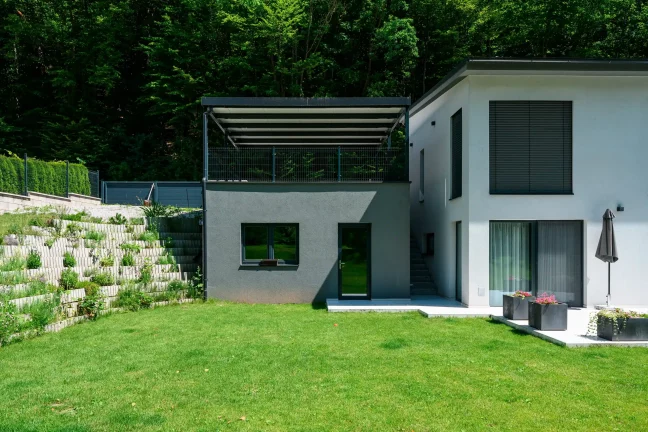 Antracitová pergola s pultovou strechou osadená na vyvýšenom podklade.