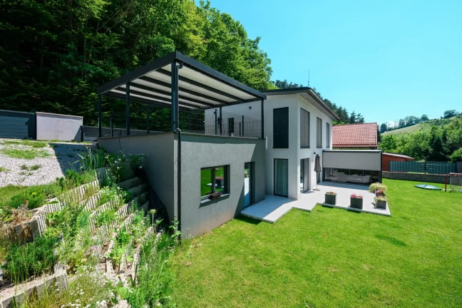 Pergola s antracitovou oceľovou konštrukciou a pultovou strechou pri rodinnom dome.