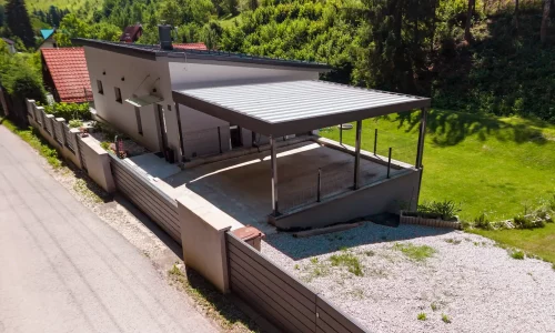 Vzdušný pohľad na prístrešok s trapézovou strechou pri bielom rodinnom dome.