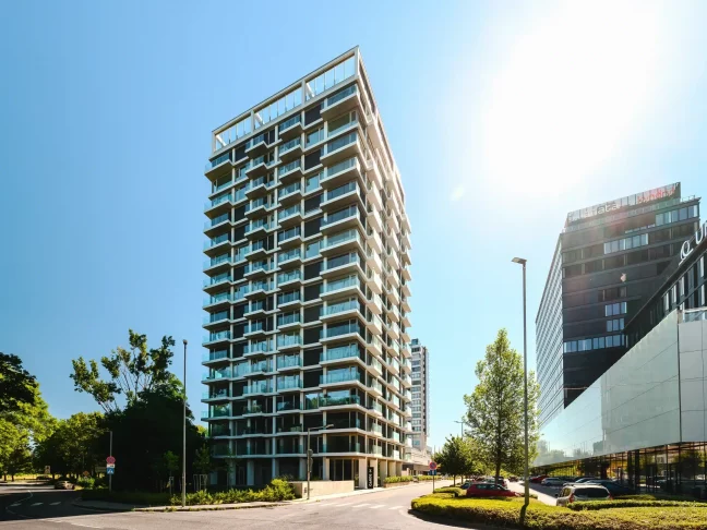 Moderná výšková budova s presklenými balkónmi a bielou konštrukciou fasády