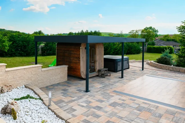 Antracitová pergola pri bazéne s priehľadným krytom, biely štrk a dláždená plocha okolo