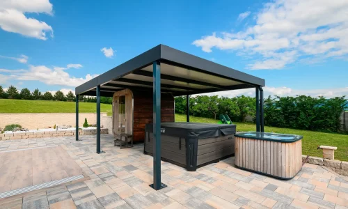 Antracitová pergola s vírivkou pod ňou na dláždenej terase, zelená záhrada a modrá obloha