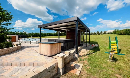 Antracitová pergola s vírivkou a detským ihriskom v pozadí, dláždená terasa pri záhrade