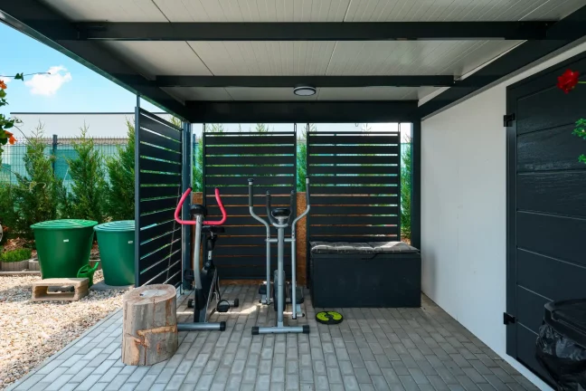 Fitnesszóna pod antracitovým prístreškom s kovovou lamelovou výplňou bočných stien.