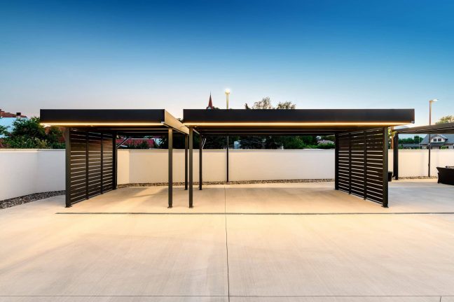 Dvojitý carport s tmavou kovovou výplňou a LED podsvietením atiky.