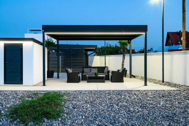 Večerná pergola s antracitovými oceľovými stĺpikmi a ratanovým sedením v záhrade.