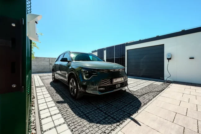 Zelené auto pripojené na nabíjaciu stanicu pri garáži