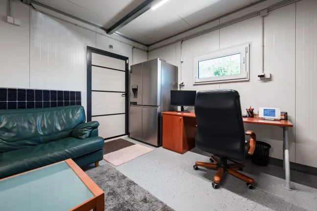 Miestnosť so zelenou sedačkou chladničkou a pracovným stolom s monitorom