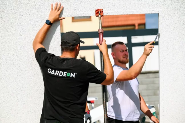 Pracovníci pritláčajú veľký stenový panel a tesnia škáru silikónom.