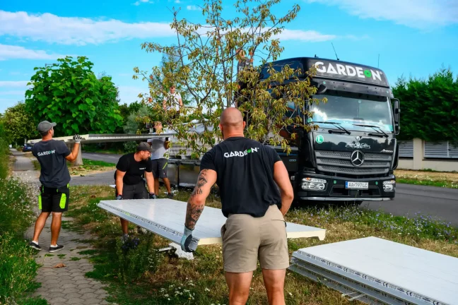 Montážnici prenášajú biele sendvičové panely od nákladiaka po tráve.