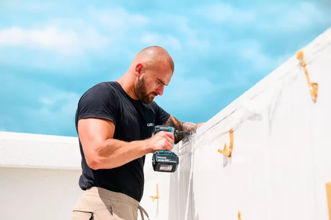 Detailný záber pracovníka vŕtajúceho do bielej strešnej lišty garáže.