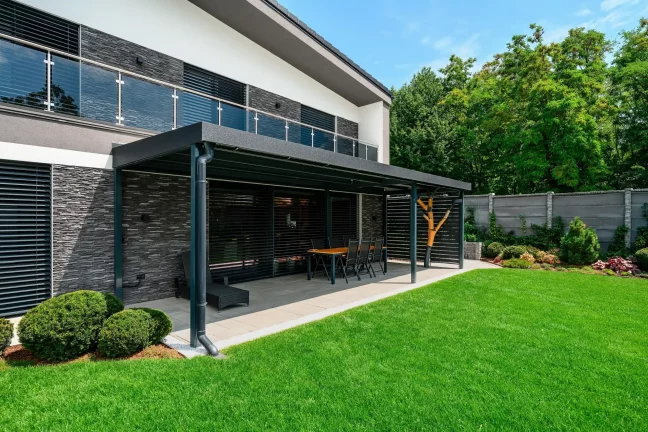 Pergola s jedálenským stolom pri dome s kamenným obkladom