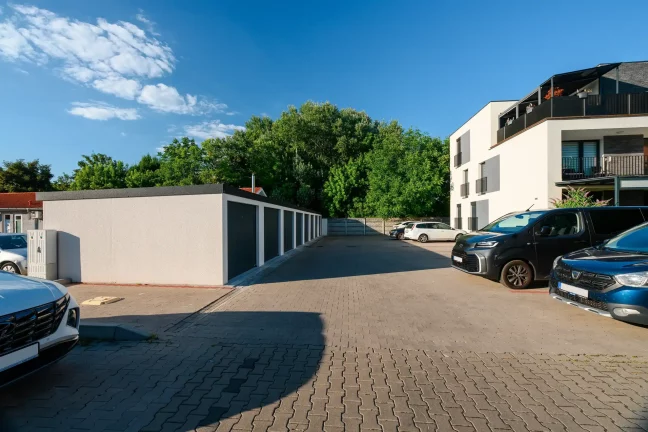 Rad garáží s parkoviskom autami a bielou bytovkou