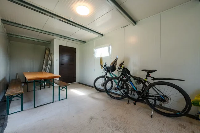 Skladová miestnosť s bicyklami, rebríkom a dreveným stolom s lavicou.