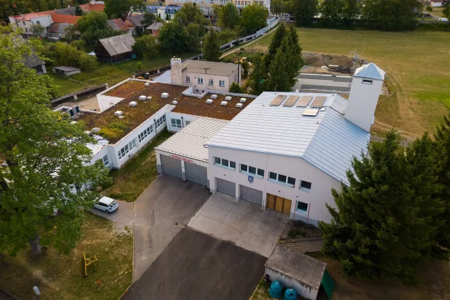 Letecký pohľad na hasičskú zbrojnicu s garážami v obci obklopenej zeleňou