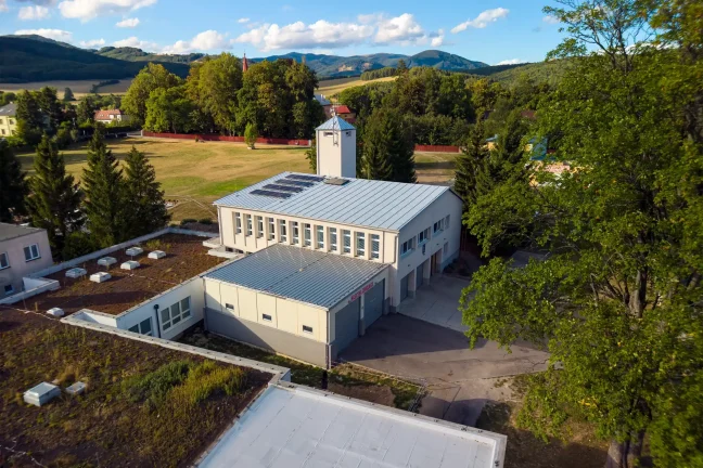 Pohľad z dronu na hasičskú zbrojnicu s novou garážou a vežou na pozadí hôr