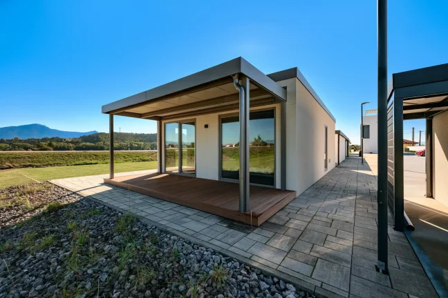 Krytá terasa tiny housu s výhľadom na hory a dláždeným chodníkom pozdĺž domu