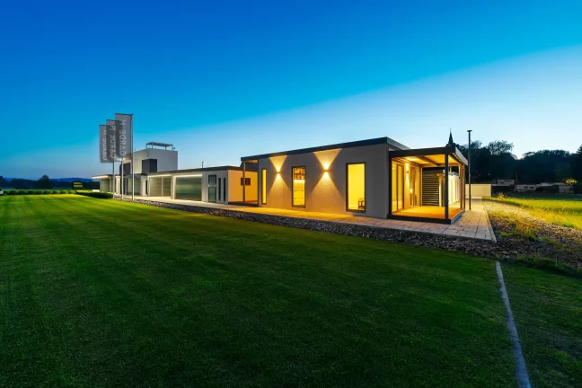 Osvetlený tiny house za súmraku, pohľad z diaľky cez trávnik